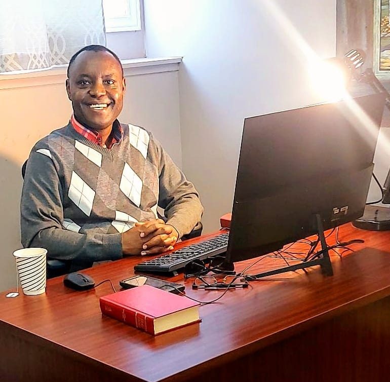 Pastor Fidele at his desk with Bible